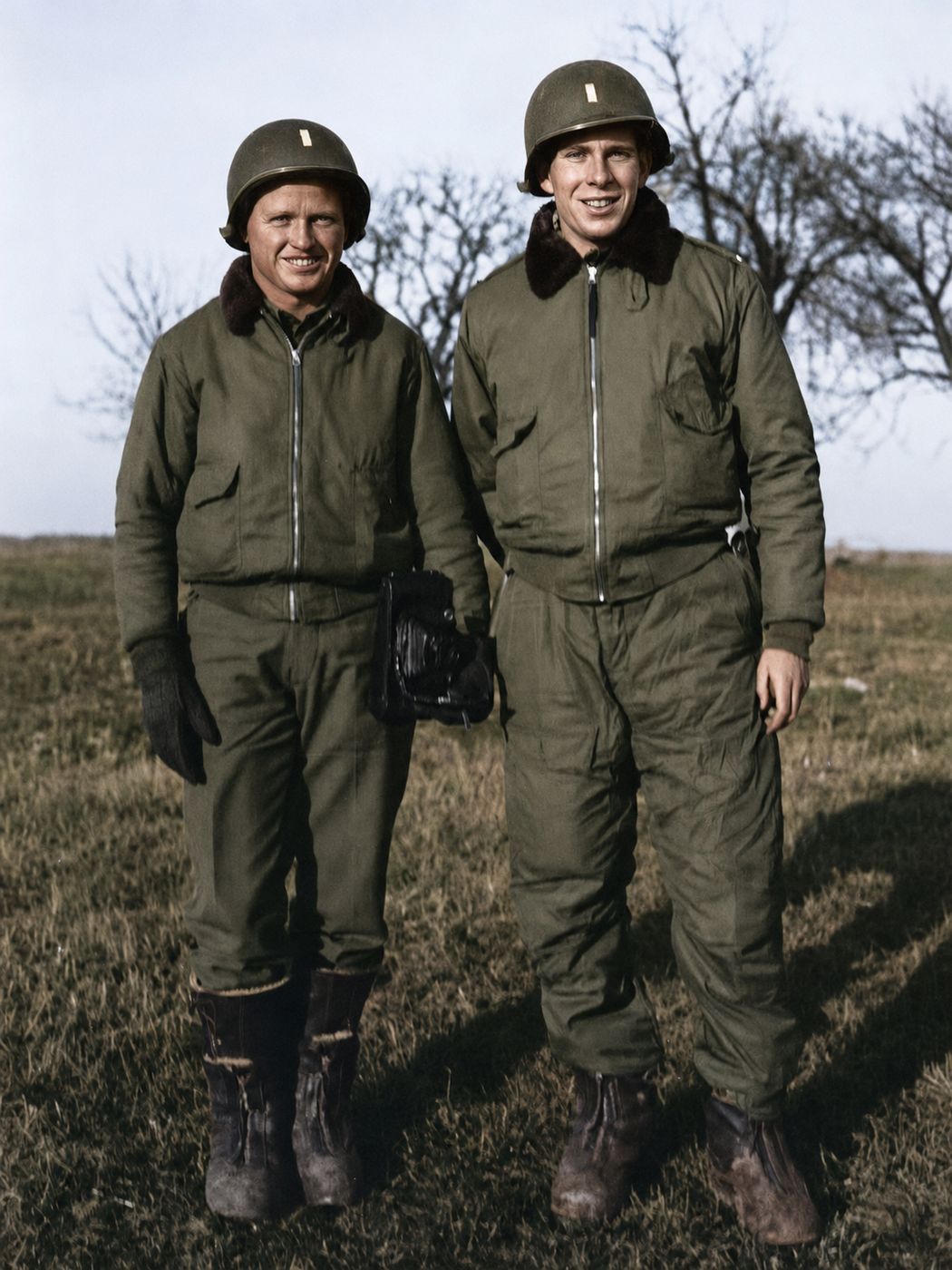 Two airmen in flight gear and helmets standing in a field